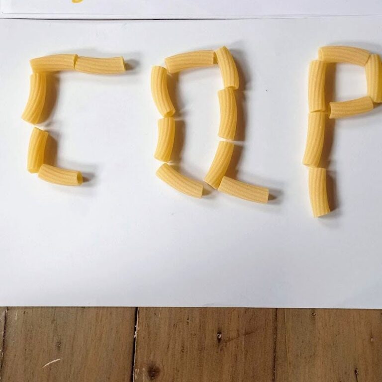 Letters made from dried pasta shapes on white paper, a hands-on way to practise letter shapes and short words